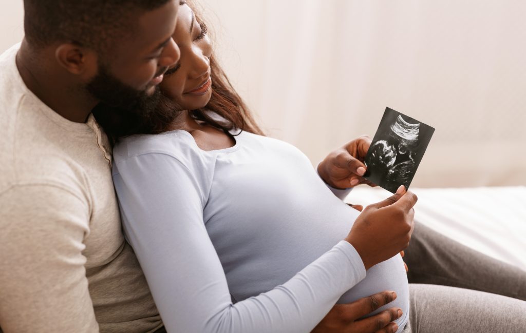 Relaxed couple watching baby ultrasound photo, lying in bed